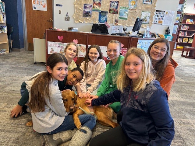 7 students smiling with a dog laying in between them