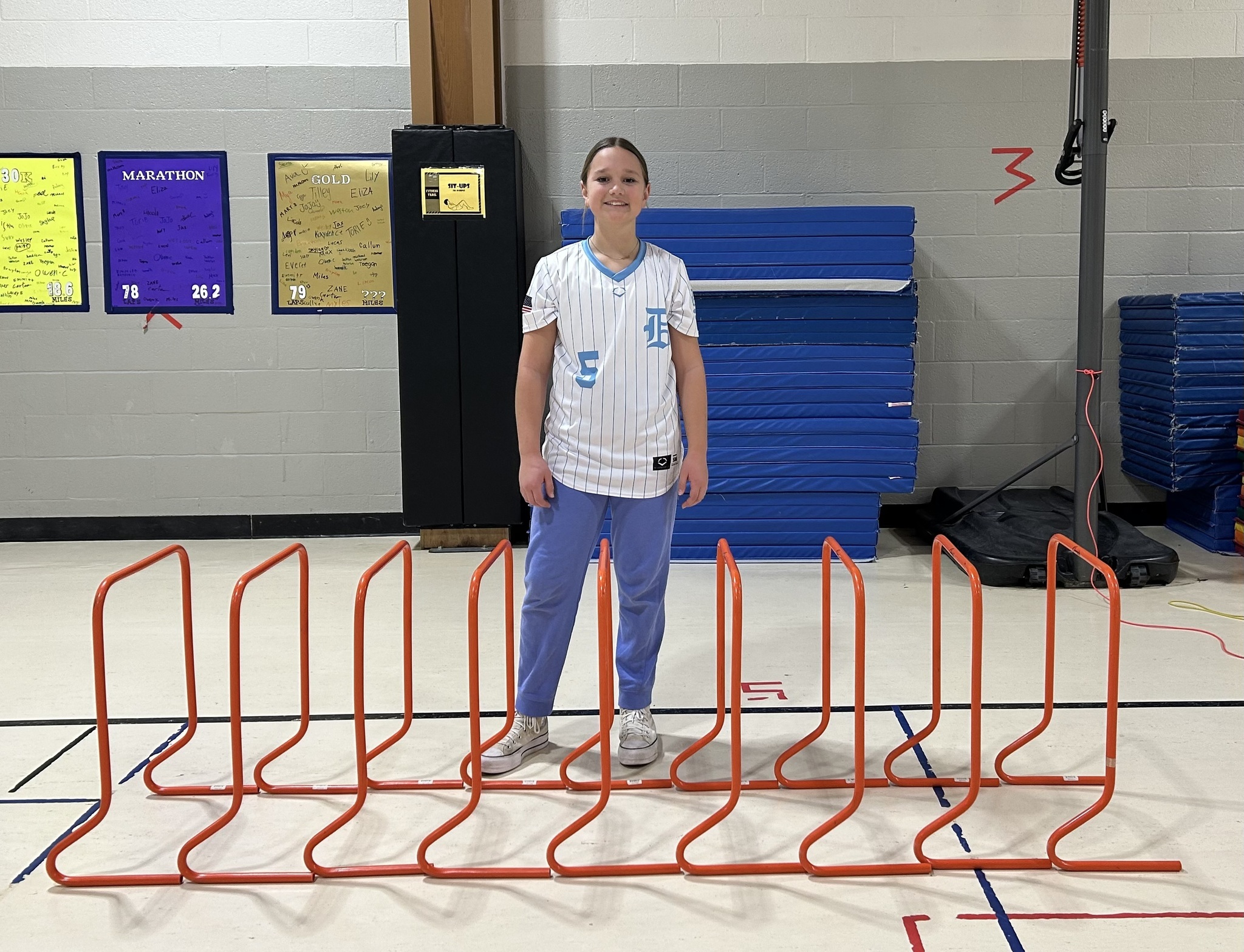 Student with blond hair stands by 9 orange hurdles